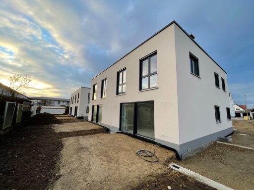 Moderne Wohnhäuser mit großen Fenstern, umgeben von neuem Erdreich und etwas Vegetation.