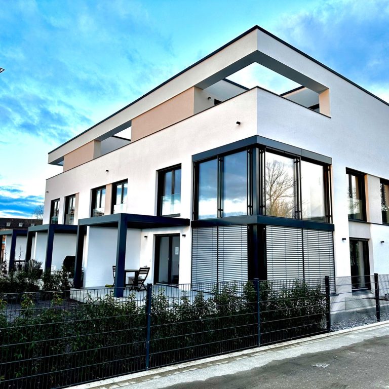 Moderne Reihenhäuser mit großen Fenstern und Dachterrassen, umgeben von Grünanlagen.