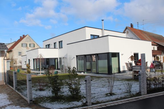 Moderner, weißer Wohnhaus mit großen Fenstern und angrenzendem Garten.