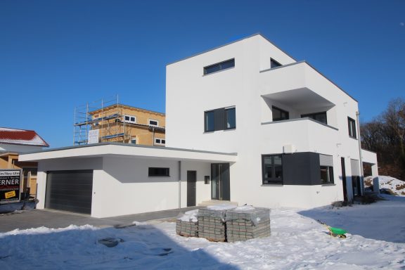 Moderne, zweigeschossige Wohnhaus mit flachem Dach und angrenzender Garage im Schnee.
