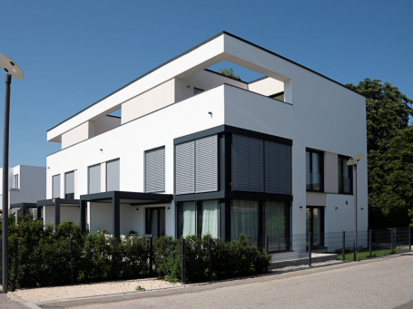 Moderne, weiße Wohnanlage mit großen Fenstern und flachem Dach in ruhiger Umgebung.