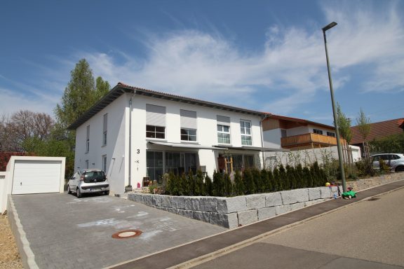 Modernes, zweigeschossiges Haus mit Garten, gepflastertem Vorplatz und Carport.