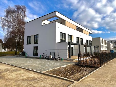 Moderne Wohnanlage mit weißer Fassade und grünen Flächen im Vordergrund.