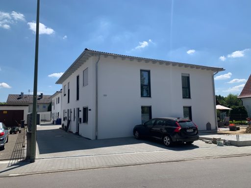 Weißes Wohnhaus mit Garten, blauer Himmel und einem schwarzen Auto auf der Auffahrt.